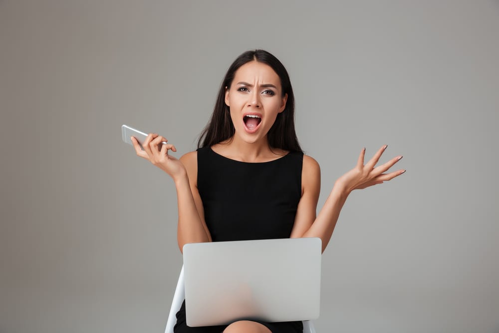 woman throwing hands up in the air with computer and phone