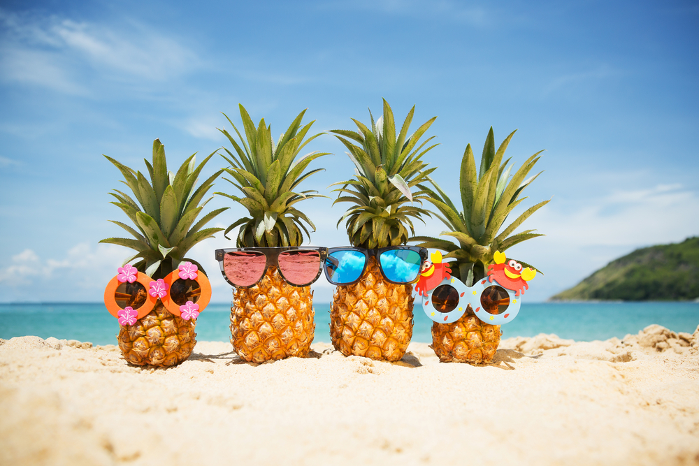 four cute summer pineapples on the beach in funny glasses
